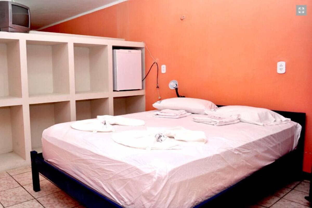 A bedroom with a bed, white pillows, and a TV on a shelf.