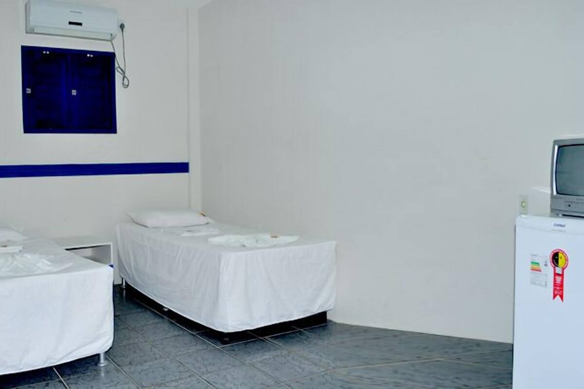A hotel room with two single beds, a small desk, a television, and a refrigerator.