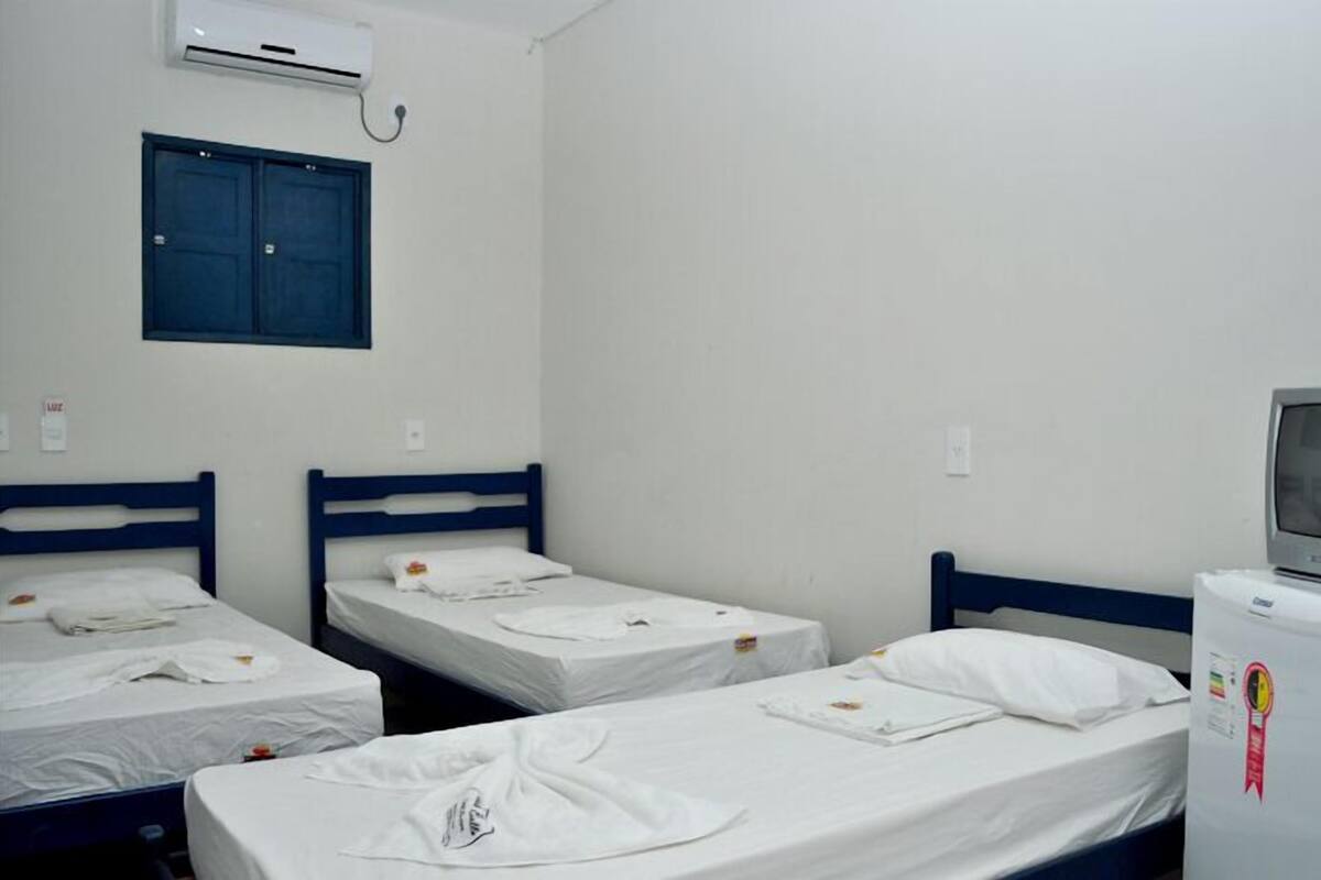 A dormitory room with three single beds, a small TV on a stand, and an air conditioning unit on the wall.