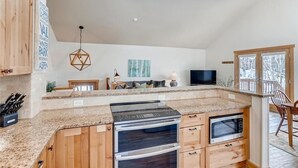 Une cuisine moderne dotée de plans de travail en granit, d’armoires en bois et d’un four encastré.