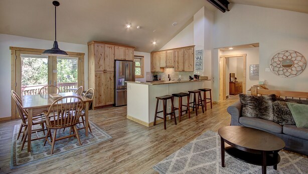 Une cuisine spacieuse dotée de meubles en bois, un îlot central avec des tabourets de bar, un coin repas avec une table et des chaises en bois, et un salon avec un canapé et une table basse.