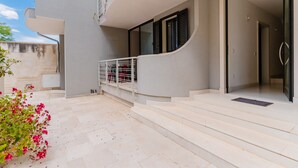 Un edificio moderno con un balcón curvo, escalones que conducen a una puerta y un pequeño jardín con flores.