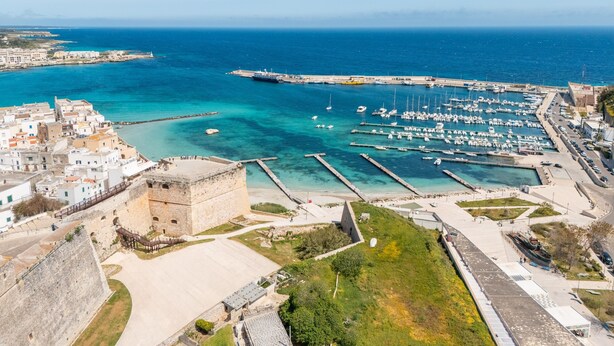 Un pueblo costero con un puerto deportivo, una fortaleza histórica y vistas claras del mar.