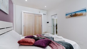 Un dormitorio con cama, almohadas, una colcha, un armario, un espejo y un cuadro en la pared.