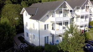 A multi-story residential building with a balcony on the second floor, surrounded by greenery.