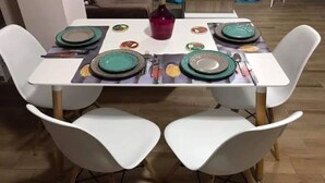 A dining table set for four with white chairs, a red bottle, and plates with a green rim. - Luxuri apartment in Masouri Armeos by Maria (Masouri)