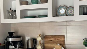 A kitchen with a coffee maker, kettle, and wooden cutting board.