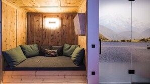 A cozy wooden cabin room with a bed, pillows, and a view of a lake and mountains. - Chalet 'Chalet Ortles' with Lake View, Private Terrace, and Wi-Fi (Sankt Valentin auf der Haide)