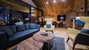 A modern living room with a wooden ceiling, a blue sofa, a round coffee table, and a dining area with chairs and a TV. - Chalet 'Chalet Ortles' with Lake View, Private Terrace, and Wi-Fi (Sankt Valentin auf der Haide)