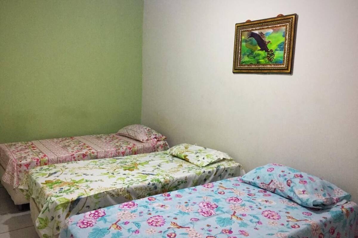 A room with two single beds, each with floral bedding, a green wall, and a framed picture on the wall.