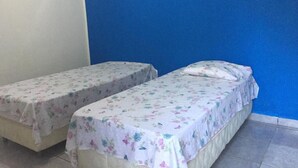 Deux lits simples, recouverts de couvre-lits à motifs floraux, dans une pièce aux murs bleus et au sol carrelé.