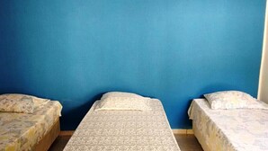 Une chambre avec deux lits simples adossés à un mur bleu, chaque lit étant recouvert d’une couvre-lit à motifs.