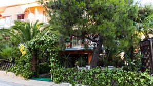 A residential building with a balcony, surrounded by lush greenery including palm trees and various shrubs. - Hotel Possidon (Aegina)