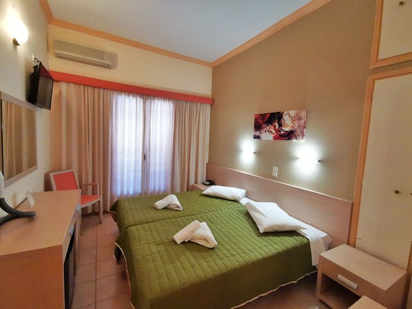 A hotel room with a bed, a desk, a chair, a TV, and a painting on the wall. - Hotel Possidon (Aegina)