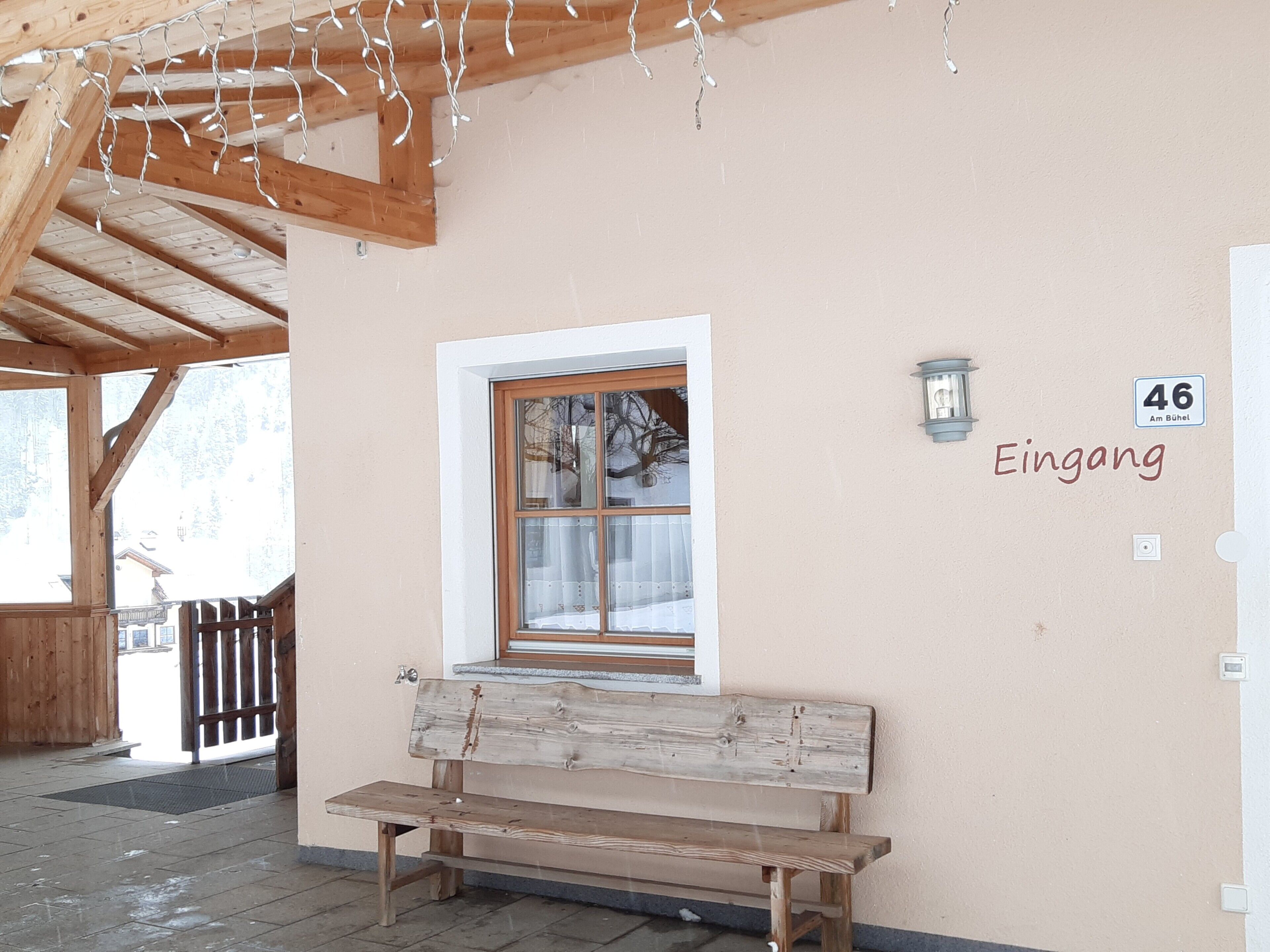 A wooden bench outside a building with a window and a wall sign reading 'Eingang.'