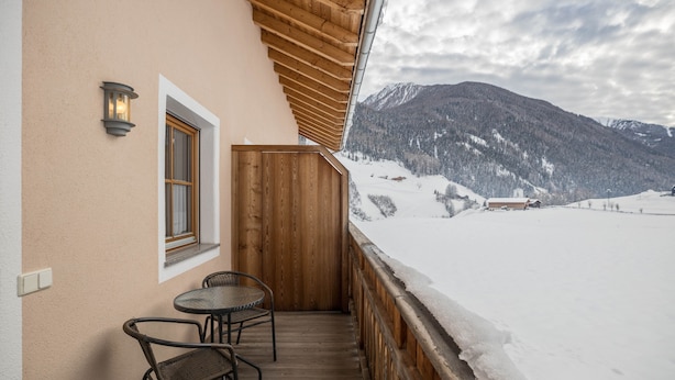 Un balcón con barandilla de madera, una mesa con sillas y vistas a montañas nevadas.