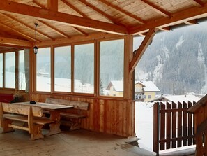 Een houten vakantiehuis met grote ramen, een bankje en uitzicht op een besneeerd landschap.