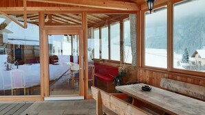 Una cabaña de madera con puerta de cristal que da al exterior, un banco en el interior y vistas a un paisaje nevado.