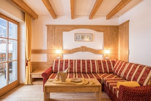Une pièce chaleureuse avec un plafond en bois, un canapé agrémenté de coussins à motifs, une table ornée d’un objet décoratif et une fenêtre avec des rideaux.