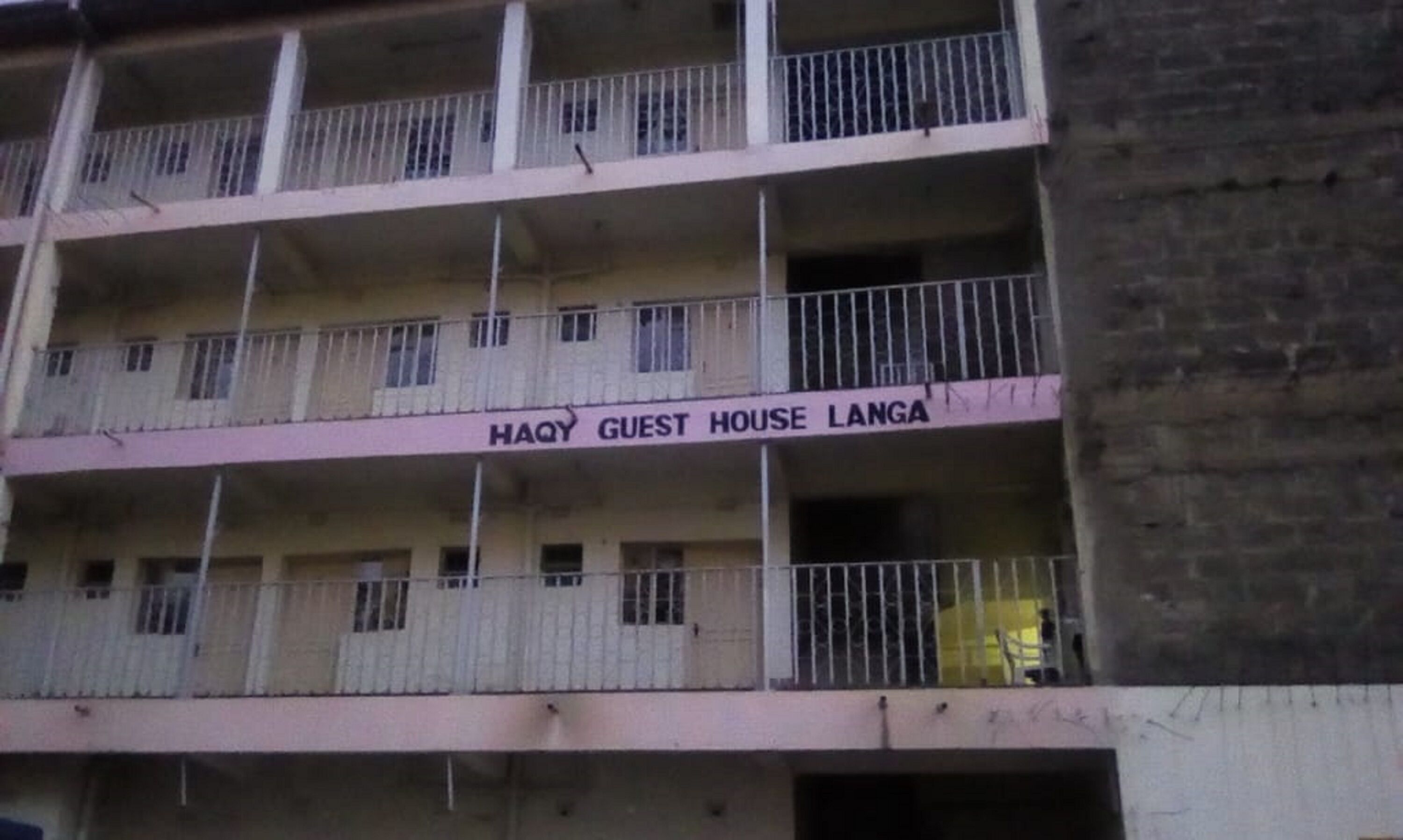 A multi-story building with balconies and a sign reading "HAQ GUEST HOUSE LANGA".