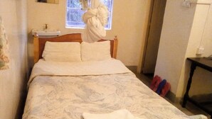 A bed with a patterned bedspread, a bedside table with a lamp, and a window with curtains. - Haqy Guest House (Nakuru)