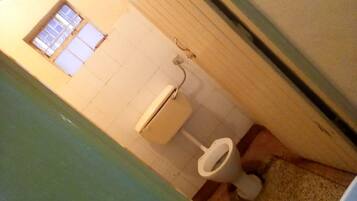 A bathroom with a toilet, a window, and a visible electrical outlet.