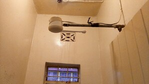 A bathroom with a ceiling-mounted shower fixture, a window with a view of buildings, and a small ventilation grille. - Haqy Guest House (Nakuru)