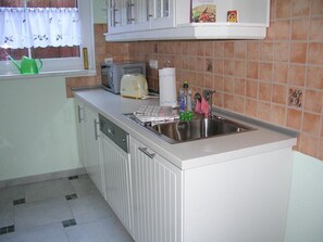 A kitchen with white cabinets, a stainless steel sink, a toaster, and a window with a curtain.