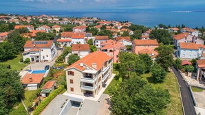 A residential area with houses featuring red-tiled roofs, a swimming pool, and a view of the sea.