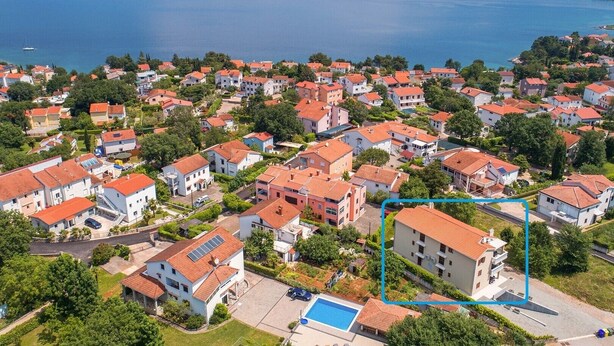 An aerial view of a residential area with houses, a swimming pool, and a body of water in the background.