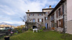 Une maison en pierre avec un petit jardin, une table blanche et une porte qui donne sur un escalier.