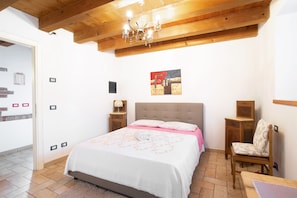Quarto com cama, uma cadeira, teto de madeira e um quadro na parede.