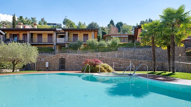 A swimming pool with a stone wall and a staircase leading to a building with balconies.