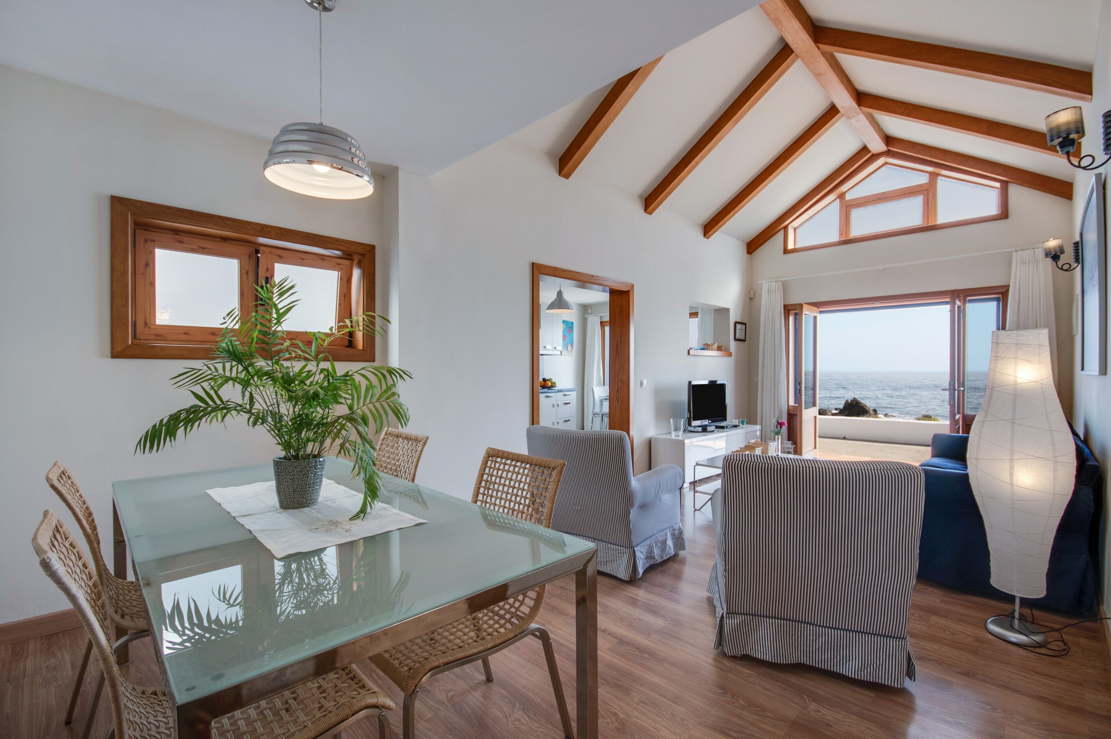A spacious living area with a glass dining table, wicker chairs, a striped sofa, and a view of the sea.