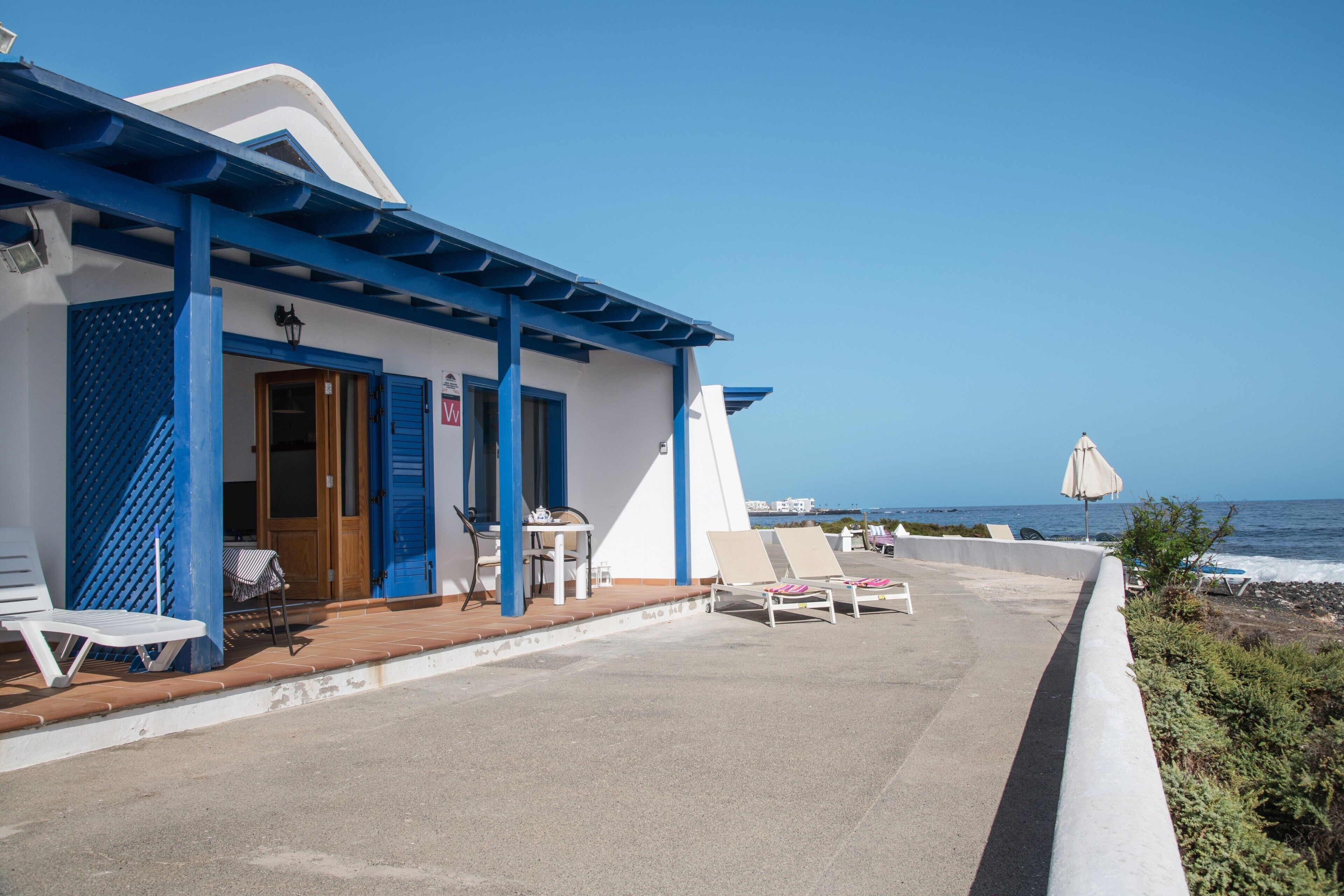 A seaside hotel with a covered patio, lounge chairs, and a view of the ocean.