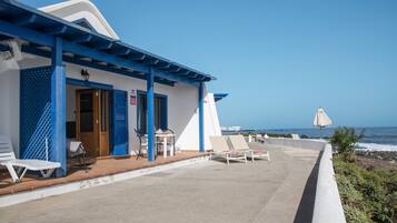 A seaside hotel with a covered patio, lounge chairs, and a view of the ocean.