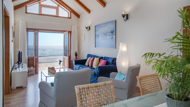 Een woonkamer met uitzicht op zee, een blauwe bank, rieten stoelen en een glazen tafel.