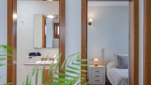 Een slaapkamer met een bed, nachtkastje, lamp en een spiegel boven de kapstok.