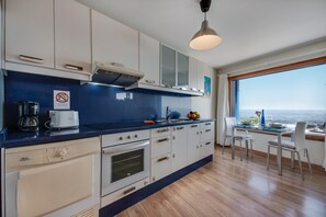 Une cuisine moderne avec vue sur la mer, un coin repas avec une table et des chaises, et une grande fenêtre.