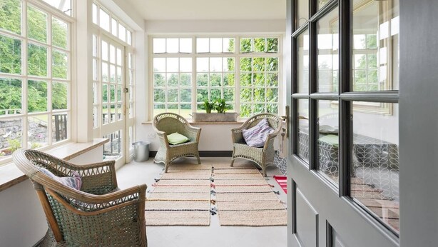 A sunlit room with large windows, wicker chairs, a small table, and a view of greenery outside. - The Manor Suite at Moyglare Manor (Maynooth)
