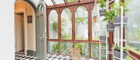 A conservatory with a checkered floor, a wooden door, and a plant rack.