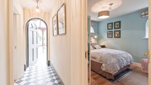 A hallway with a checkered floor leading to a bedroom with a bed, a nightstand, and a wall with framed pictures. - The Manor Suite at Moyglare Manor (Maynooth)