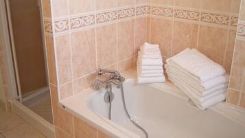A bathroom with a bathtub, a shower, and a stack of white towels.