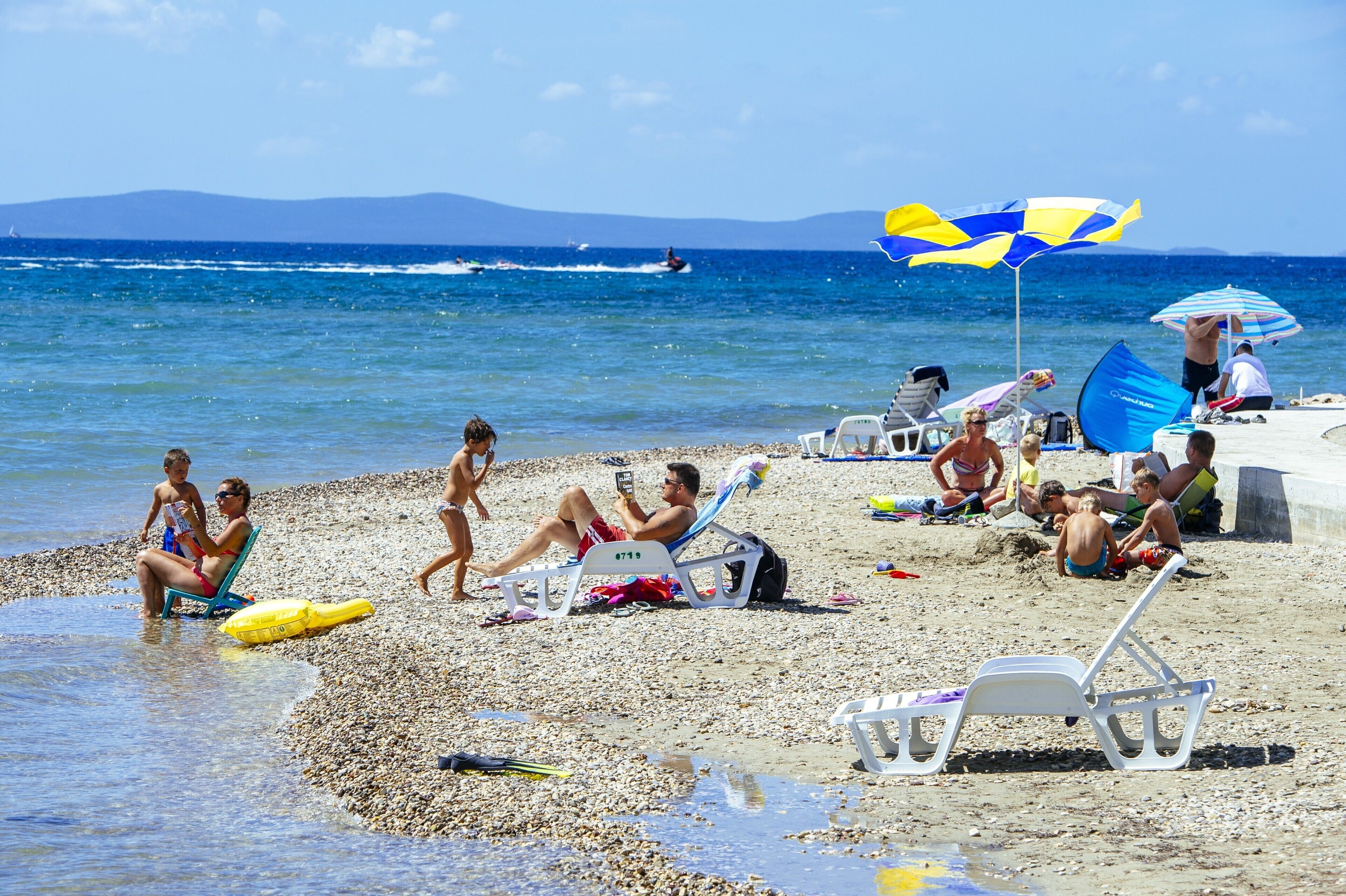 Una playa con gente tomando el sol y nadando, y un jet ski en el agua.