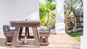 A wooden outdoor table with chairs, a tiled patio, and a white wall.