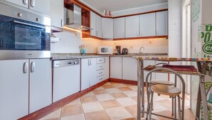 Cozinha com armários brancos, forno de aço inoxidável, micro-ondas e cafeteira.