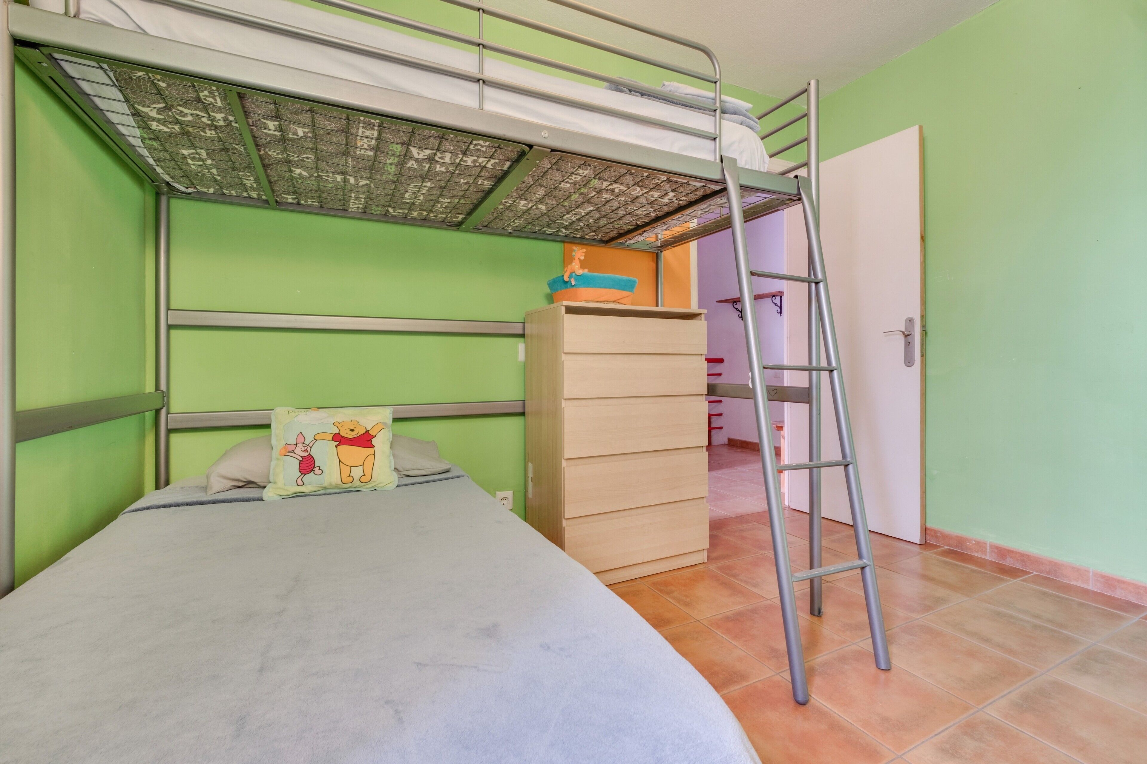 Ein Stockbett mit einer Leiter, eine Kommode und eine Tür in einem Zimmer mit grünen Wänden.