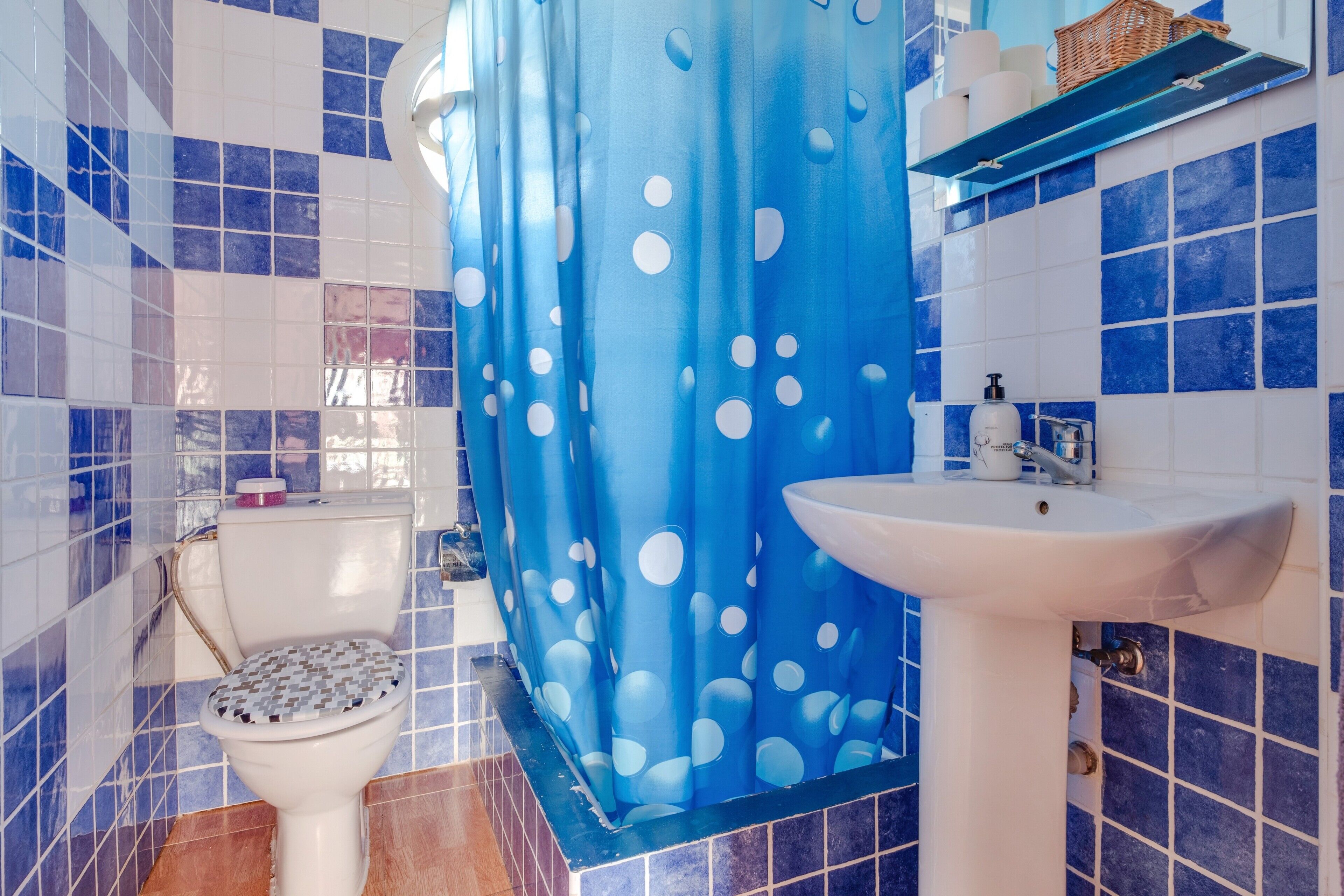 Une salle de bain avec des carreaux bleus et blancs, des toilettes, un lavabo et un rideau de douche à pois blancs.