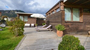 A wooden cabin with a deck, two lounge chairs, a white umbrella, and potted plants. - Holiday Apartment "GeoResort B6" with Panoramic Views and Shared Pool (Tremosine)
