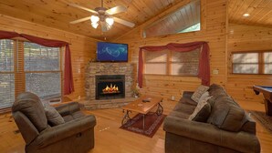Un acogedor interior de cabaña con una chimenea de piedra, dos sofás, una mesa de centro y un televisor de pantalla plana montado sobre la chimenea.